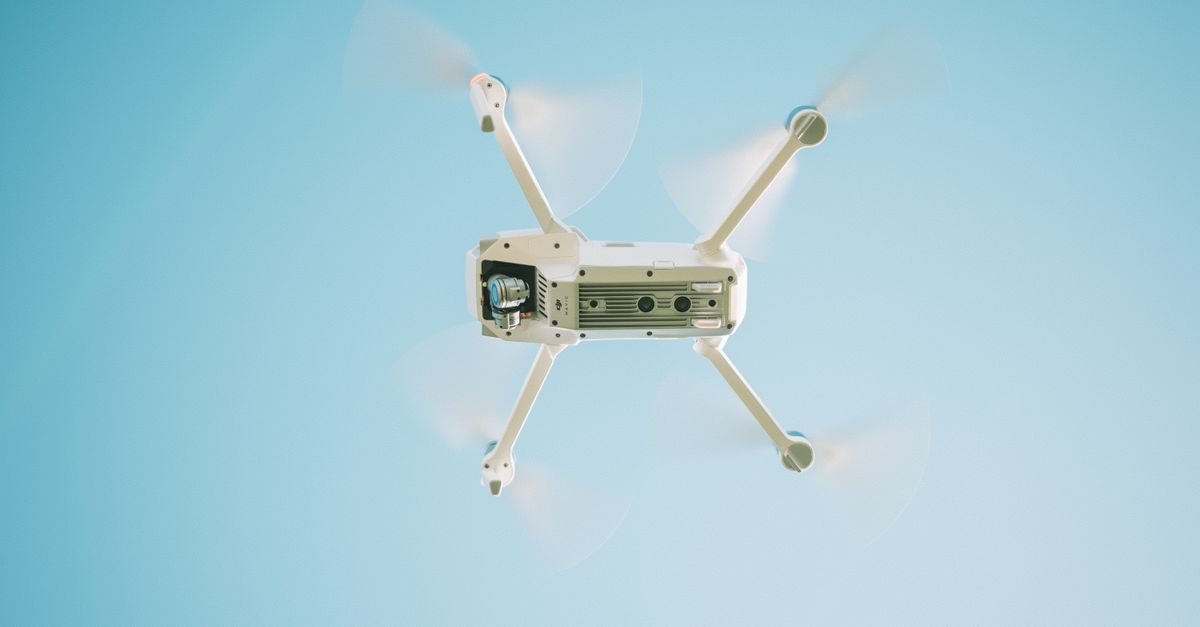 A sleek white drone flying under a clear blue sky, capturing aerial views.