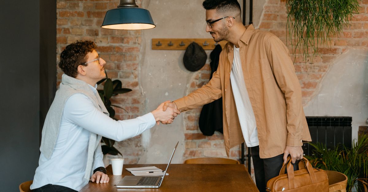 Two businessmen shake hands in a modern office setting, sealing a partnership.