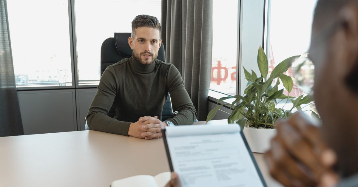 Professional man in turtleneck at office desk during an interview.