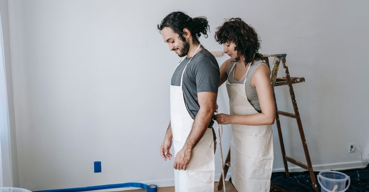 A couple enjoying time together painting a room. They are wearing aprons and working on home renovation.
