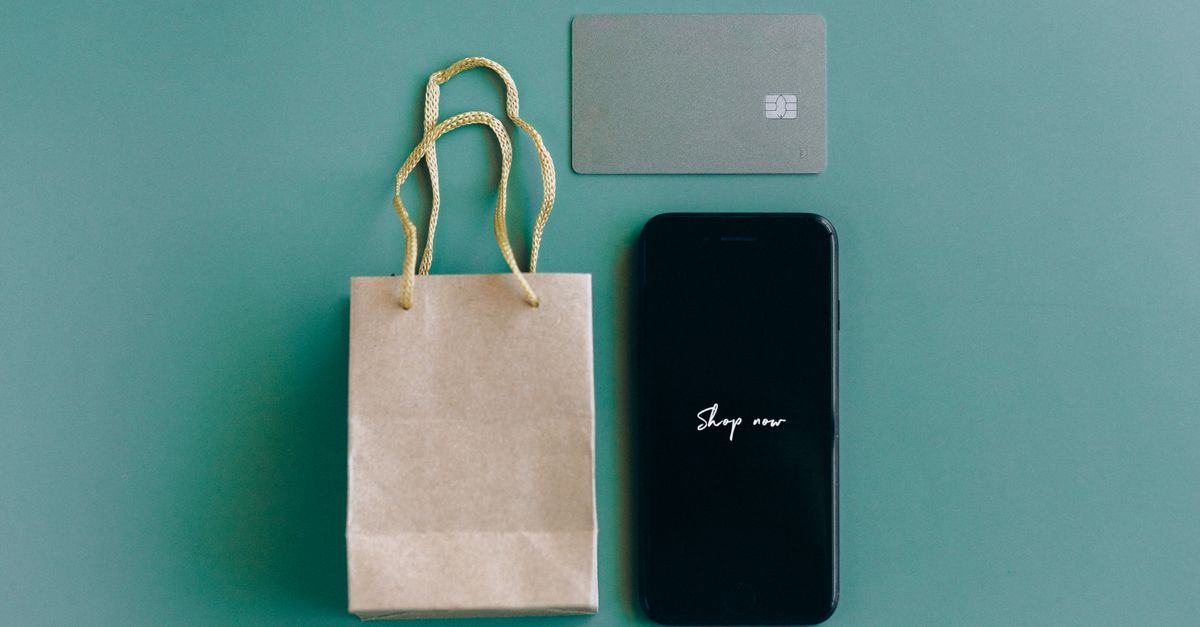 Top view of smartphone with 'Shop now' text, credit card, and paper bag on green background.